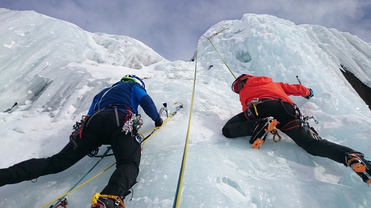 Photo of two ice climbers scaling an ice wall. Harnesses attached.