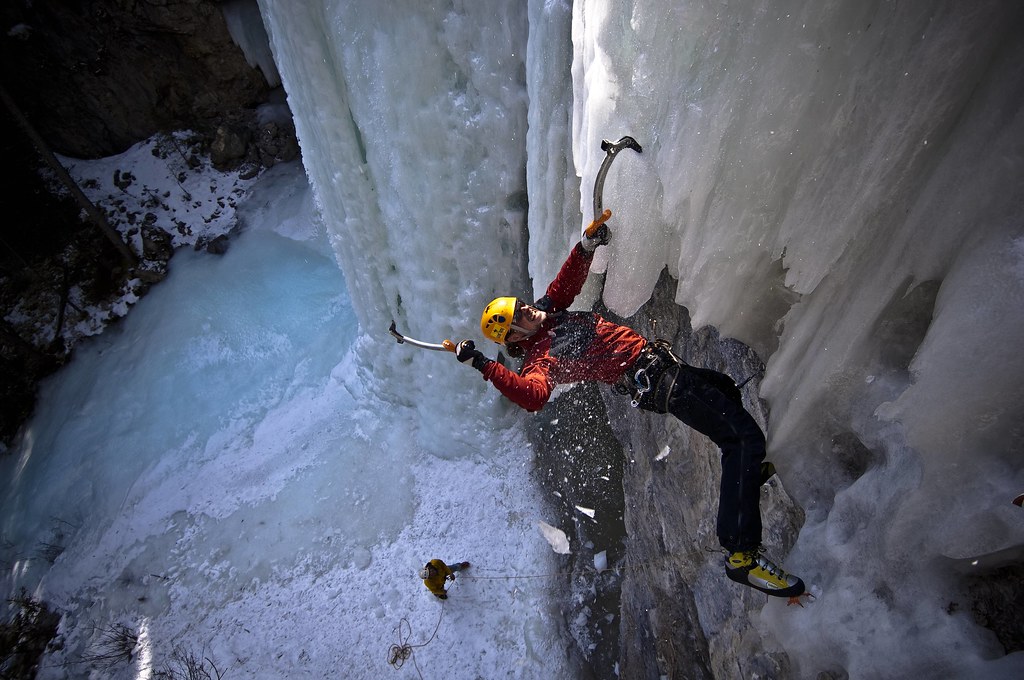 Photo of an ice climber hanging from the ice waterfall using ice climbing picks.
