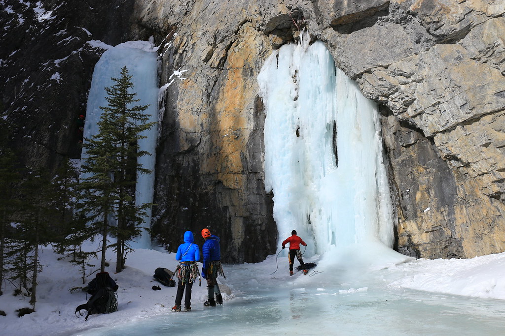 Photo of Ice Climbing Victoria members standing in front of a climbing waterfall with trees and water in the scene